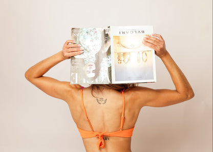 Women wearing an orange underwire bikini holding a magazine with a beige studio background
